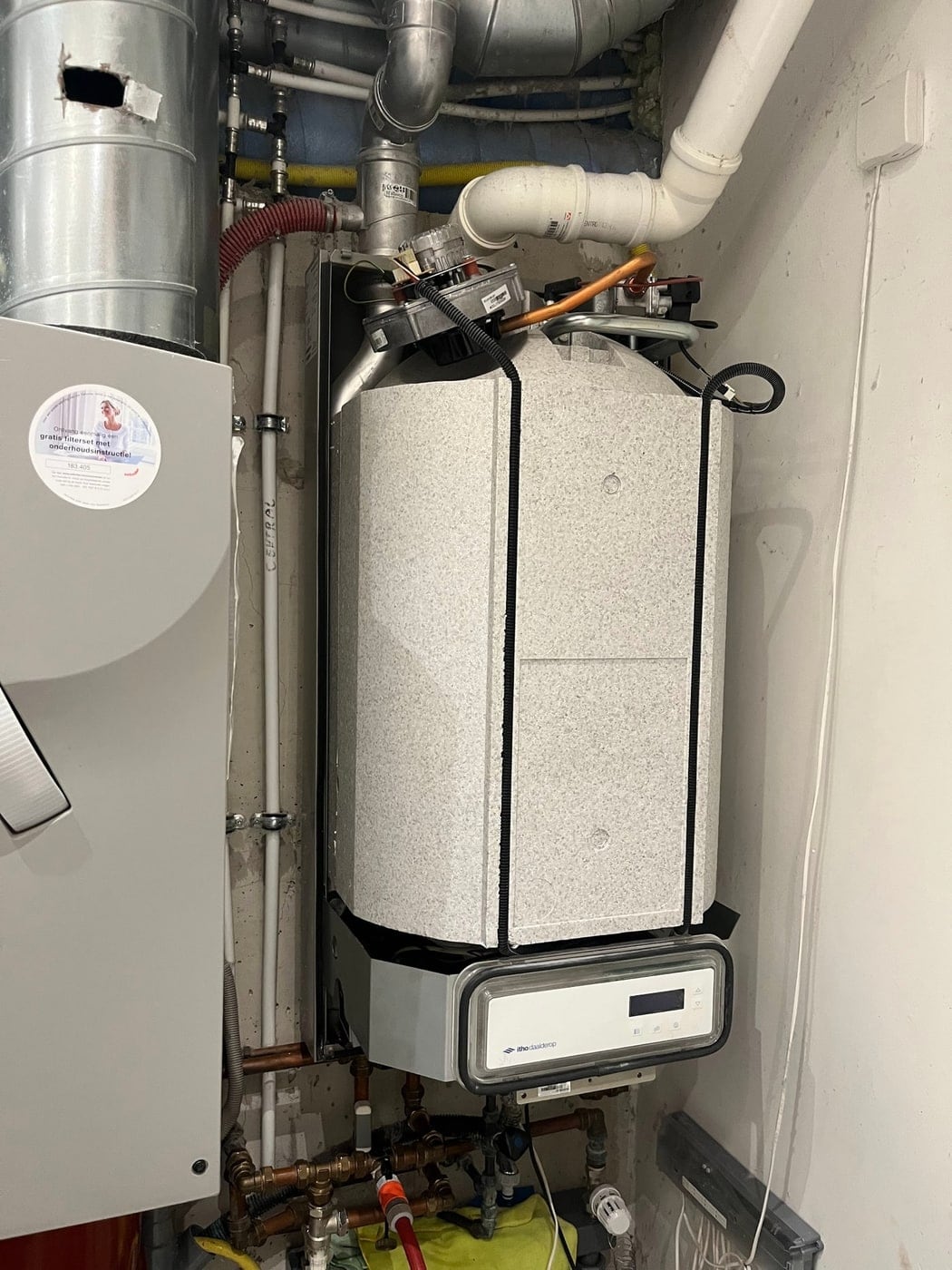Cv-ketel met rookgasafvoer, ventilatiekanalen en koperen leidingwerk in een technische kast, met daaronder een Itho Daalderop ventilatie-unit.