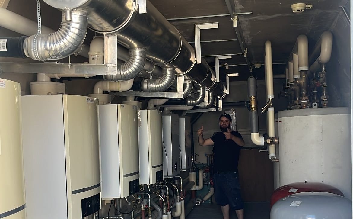 Technische ruimte met acht cv-ketels in cascade-opstelling, aangesloten op geïsoleerde leidingen en een expansievat. Ömer van Macka Installatie staat tussen de installatie.